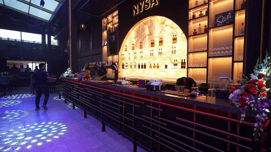 A vibrant bar showcasing a display of alcohol on shelves, set in a lively atmosphere with bartenders preparing drinks at Nysa Skybar, Bengaluru.