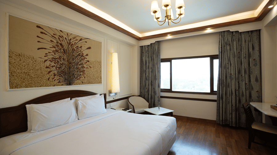 A king size bed with crisp linens sits beneath a floral wall panel and a decorative chandelier in the Deluxe King room at Clarks Amer, Jaipur.