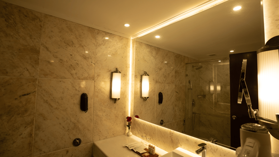 A large back-lit mirror and a rectangular vessel sink sit on a white countertop in the Deluxe King bathroom at Clarks Amer, Jaipur.
