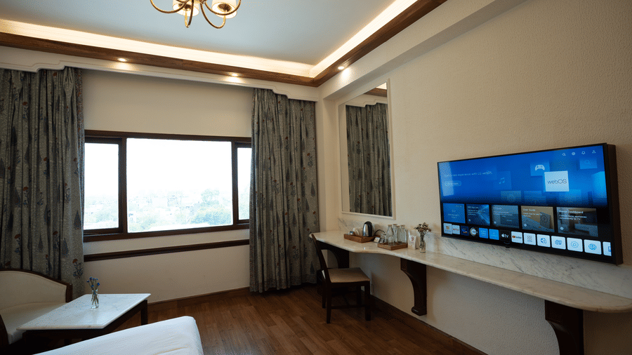 A wall-mounted flat screen television and a long wooden desk face the bed in the Deluxe King room at Clarks Amer, Jaipur.
