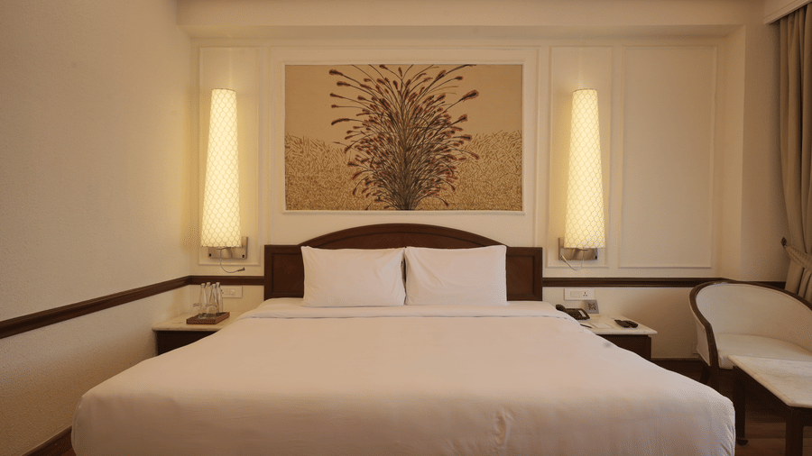 A double bed with a decorative wall panel and vertical light fixtures sits center stage in the Superior King room at Clarks Amer, Jaipur.