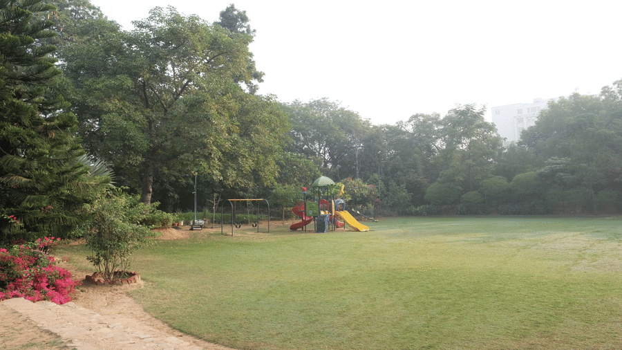 A colourful children's play area sits on a wide lawn surrounded by lush green trees in a peaceful park setting - Clarks Amer, Jaipur