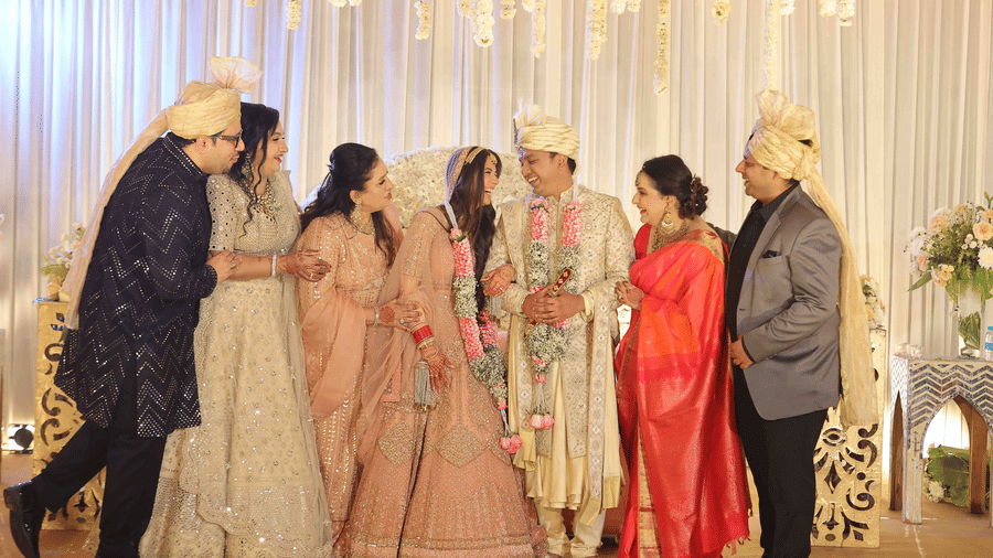 The bride and groom sharing a joyful moment with family members on a beautifully decorated wedding stage during a traditional wedding ceremony | Clarks Amer, Jaipur