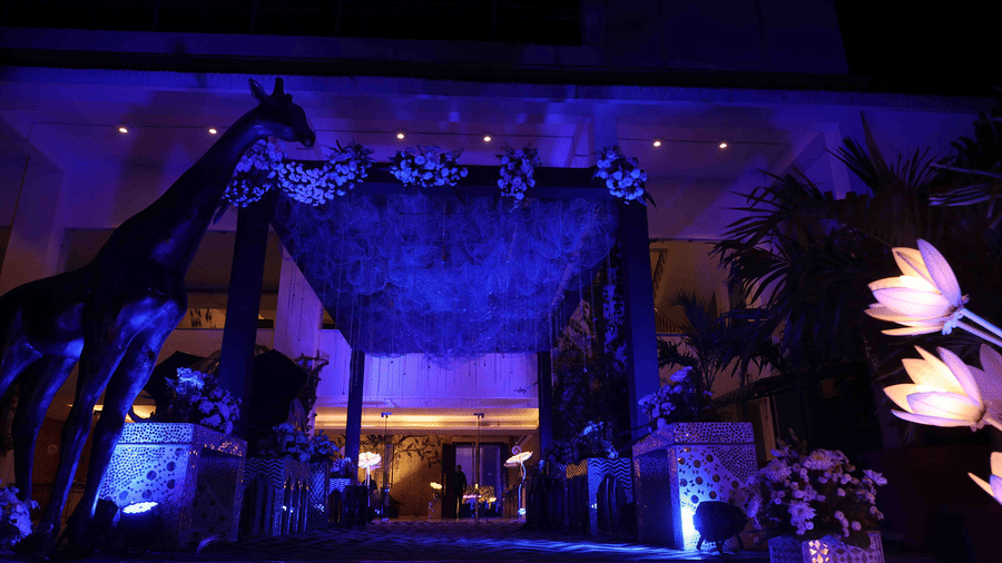A grand wedding entrance adorned with floral arrangements, ambient blue lighting, decorative installations, and elegant event styling welcoming guests to the celebration at Clarks Amer, Jaipur.
