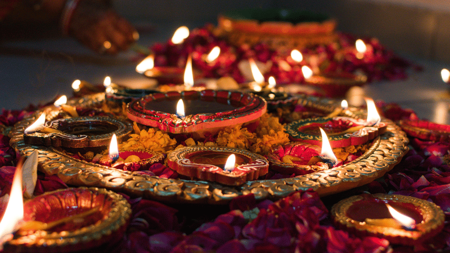 Small oil lamps lit during a hindu festival and the lamps are surrounded with flowers and loose petals.
