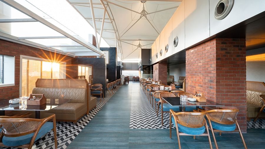 A restaurant interior with a long dining area lined with tables and chairs. The floor is tiled in a black and white geometric pattern - Clarks Inn, Indore