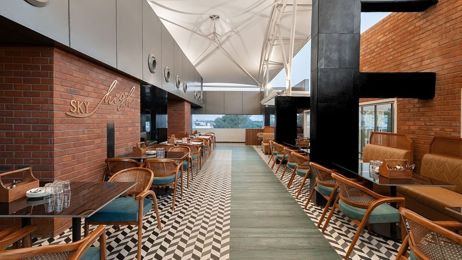A modern restaurant interior with a long dining area lined with tables and chairs. The floor is tiled in a black and white geometric pattern - Clarks Inn, Indore
