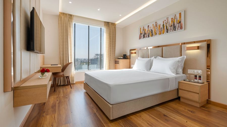 Interior view of a hotel room featuring a king size bed, a flat-screen TV, a work desk, and a large window - Clarks Inn, Indore