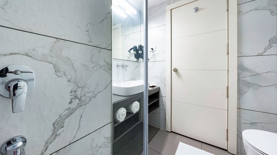 A modern hotel bathroom with a white sink, toilet, and shower. The walls are tiled with a marble pattern -  Clarks Inn, Indore