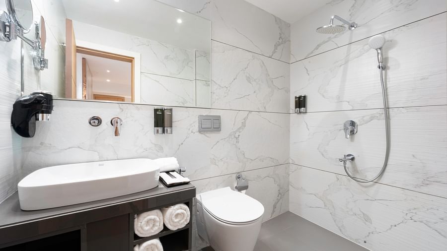 A spacious bathroom with white marble-look tiles, a walk-in shower, a sink, and a toilet -  Clarks Inn, Indore