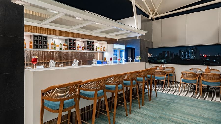 A modern rooftop bar with a long white bar, a row of high chairs, and a view of the city at night - Clarks Inn, Indore
