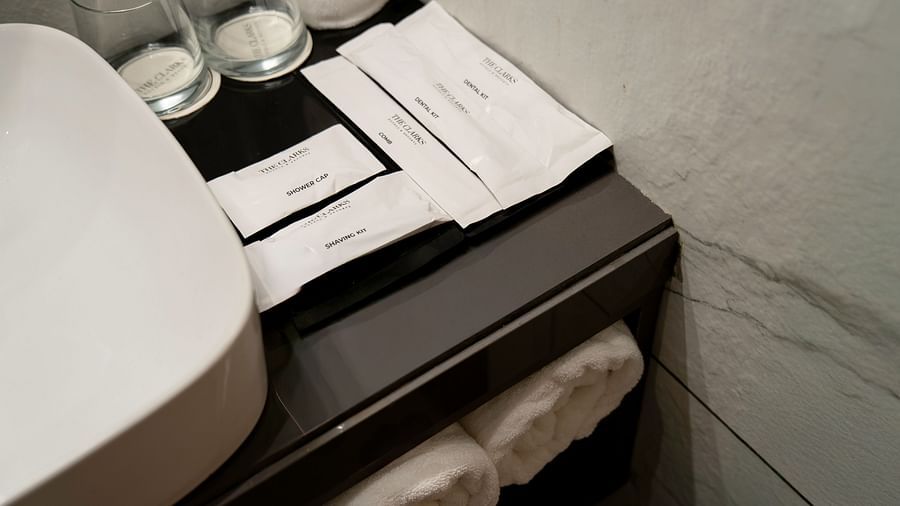 A bathroom vanity with a white sink, rolled towels, and a variety of toiletries including dental kits, shower caps, and shaving kits - Clarks Inn, Indore