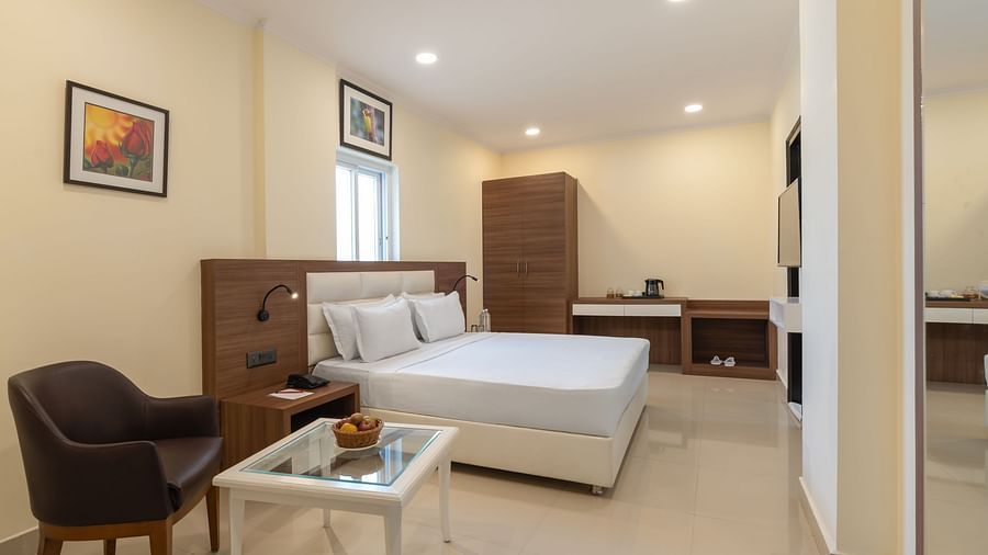 Executive Room at Clarks Inn, Near Kainchi Dham featuring a double bed with white linens, a brown armchair, a glass-topped table, and a wooden wardrobe.