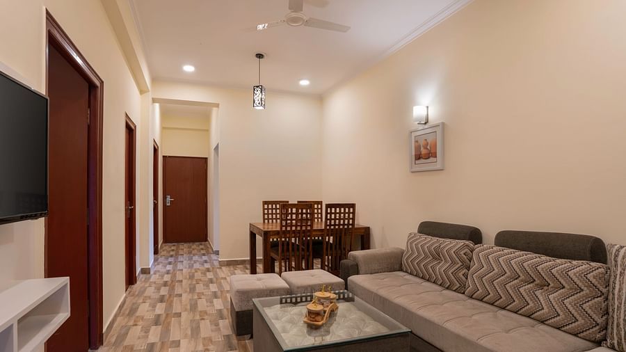 Family Apartment Room Valley View featuring living area features a grey sofa, a glass coffee table with pouffes, a dining table with chairs, and doorways leading to other rooms at Clarks Inn, Near Kainchi Dham.