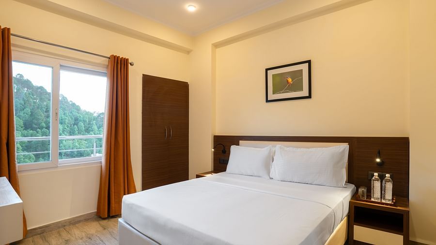 Family Apartment Room Valley View shows a double bed with white bedding, bedside tables, a wardrobe, a window with orange curtains, and a framed picture on the wall at Clarks Inn, Near Kainchi Dham.