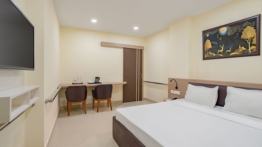 Accessible room at Clarks Inn, Near Kainchi Dham shows a double bed with white bedding, a wall-mounted television, a desk with two chairs, and a framed painting above the bed.