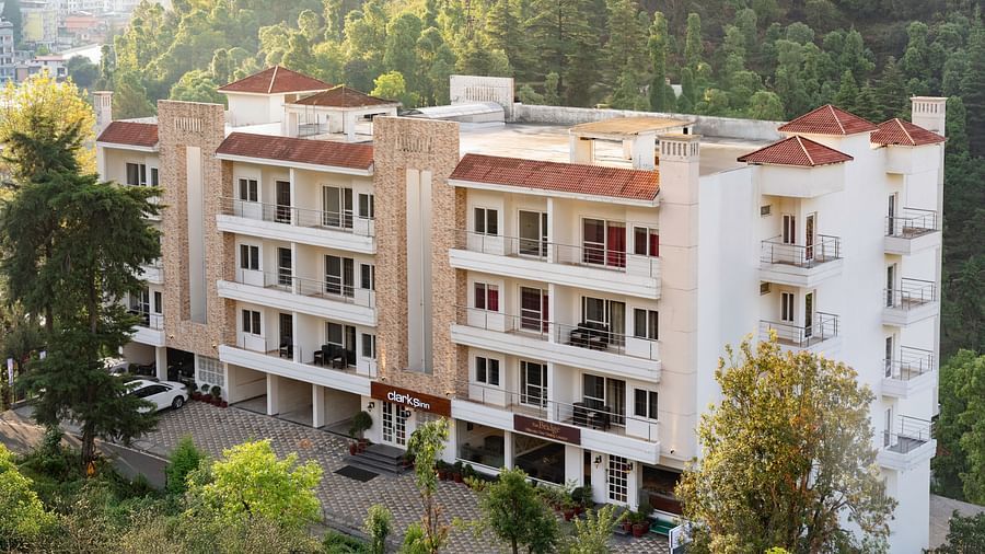 Facade of Clarks Inn, Near Kainchi Dham in Bhowali, nestled amongst trees with a view of surrounding hills.