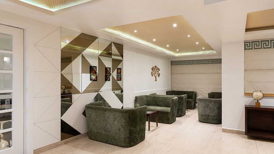 Lobby of Clarks Inn, Near Kainchi Dham features plush green armchairs, mirrored geometric wall panels, decorative gold accents, and recessed lighting in the ceiling