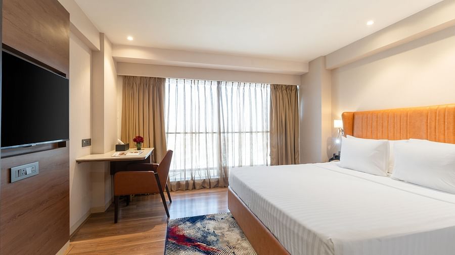 Bright hotel room with large bed, wooden floor, desk and window with sheer curtains at Clarks Inn Suites, Hyderabad