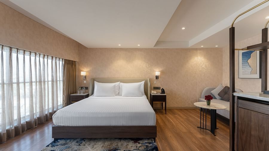 Contemporary room featuring plush bedding, lounge seating, wood flooring, and elegant lighting with a framed painting at Clarks Inn Suites, Hyderabad