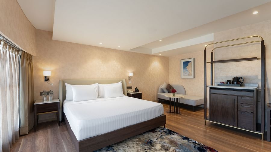 Corner suite with a king-size bed, minibar setup, soft lighting, decorative rug, and chic seating by large windows at Clarks Inn Suites, Hyderabad