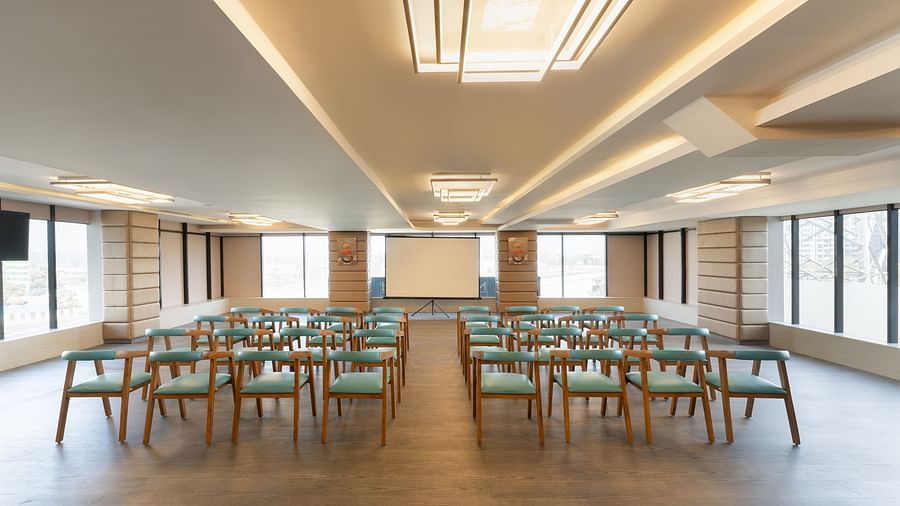 Modern conference hall with rows of wooden chairs facing a projector screen at Clarks Inn Suites, Hyderabad