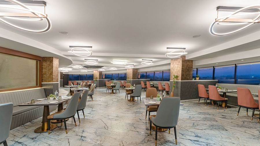 Spacious restaurant interior featuring marble flooring, grey and terracotta chairs, panoramic windows overlooking city skyline at Clarks Inn Suites, Hyderabad