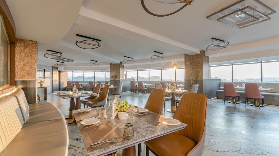 Cosy dining setup with curved banquette seating, marble tables, leather chairs and decorative ceiling lights at Clarks Inn Suites, Hyderabad