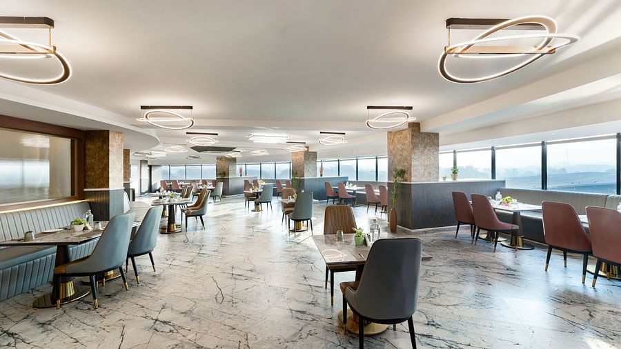Bright restaurant dining area with marble floor, pastel and brown upholstered chairs, floor-to-ceiling windows and modern pendant lights at Clarks Inn Suites, Hyderabad