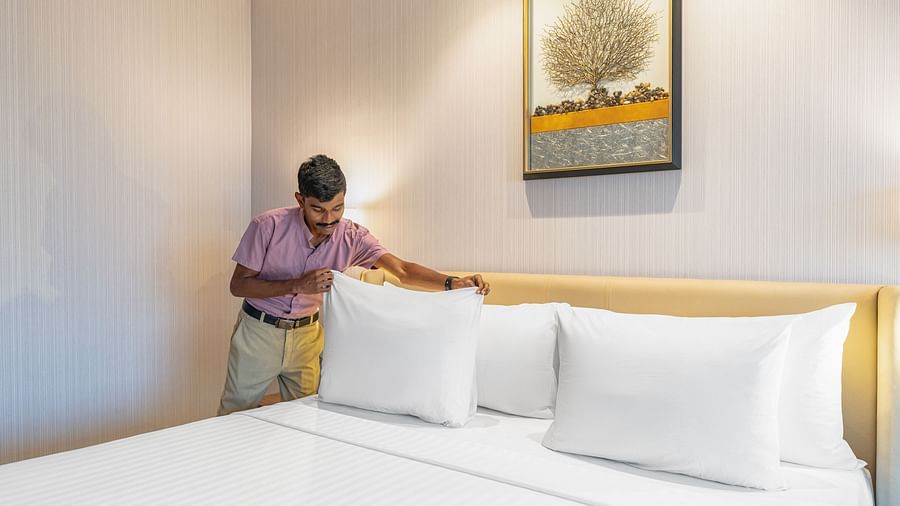 Uniformed staff member smoothing crisp white sheets on a king-size bed in a neutral-toned bedroom at Clarks Inn Suites, Hyderabad
