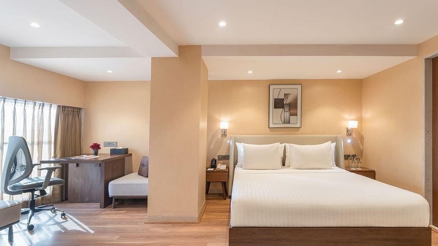 Elegant hotel room with plush king-size bed, soft lighting, wood flooring, and a study area with an office chair at Clarks Inn Suites, Hyderabad