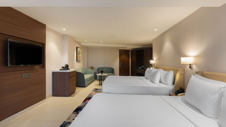 Hotel room with two queen beds, a cosy sofa, TV unit and muted lighting for a relaxed ambience at Clarks Inn Suites, Hyderabad