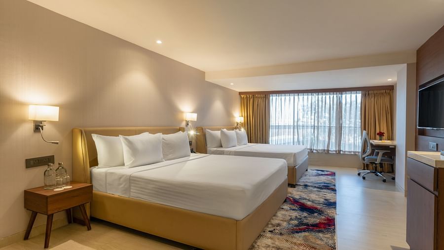 Brightly lit hotel room with two queen beds, patterned rug and desk space near a large window at Clarks Inn Suites, Hyderabad