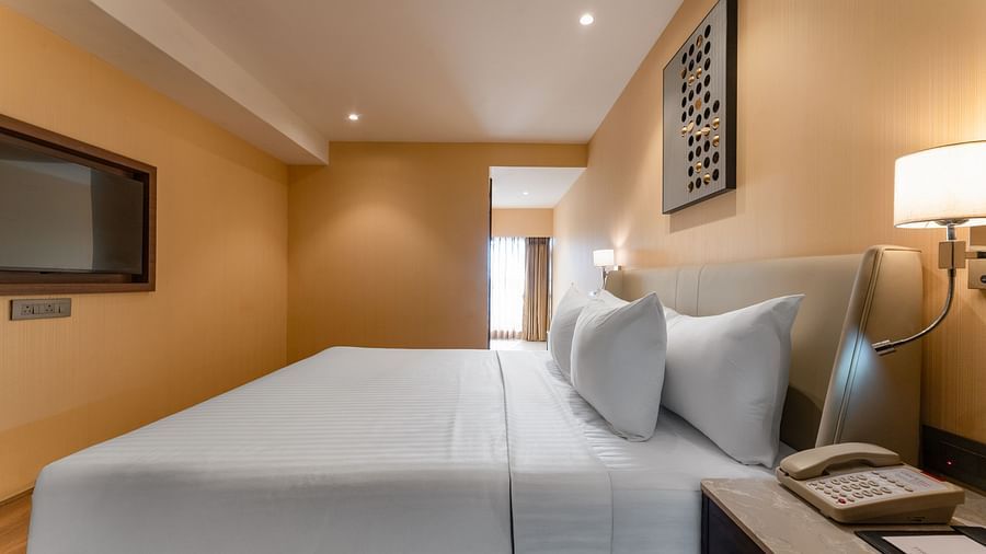  Side view of a double bed with wall-mounted TV and nightstand in a warm-lit bedroom at Clarks Inn Suites, Hyderabad