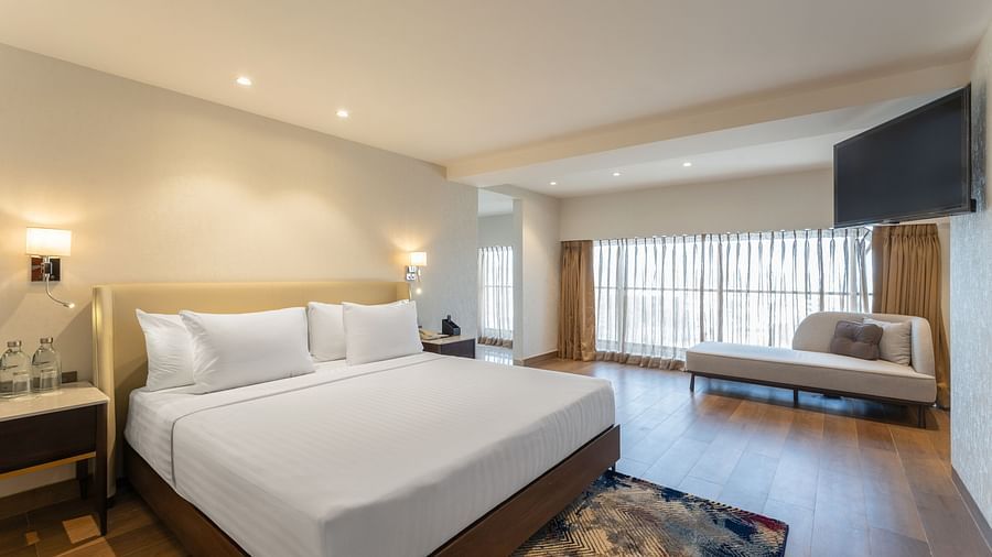 Luxurious hotel suite with king-size bed, soft ambient lights, chaise lounge by the window, and an accent rug at Clarks Inn Suites, Hyderabad