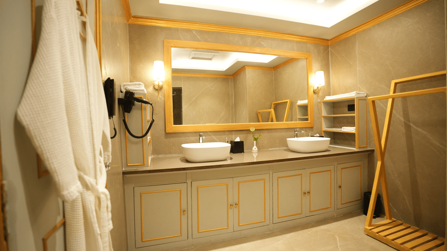 An Executive Suite bathroom at Clarks Khajuraho with dual sinks, a large mirror, bathrobes hanging on hooks, and a spacious vanity counter.