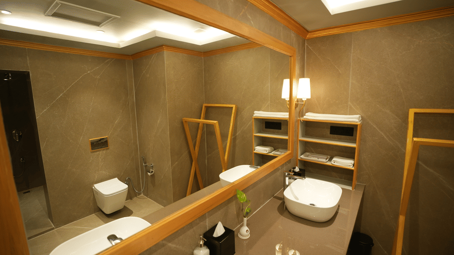 An Executive Suite bathroom at Clarks Khajuraho featuring a vanity counter with a sink, a wall-mounted mirror, a toilet, and warm ambient lighting.