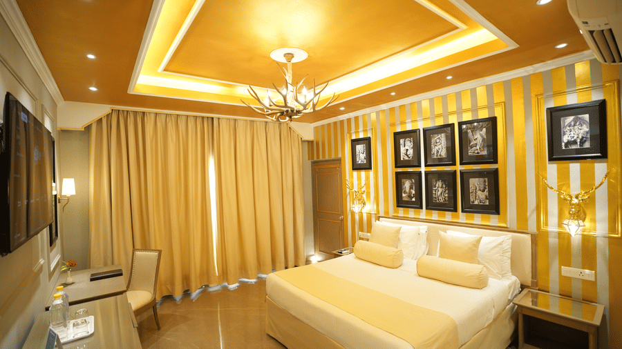 An Executive Suite bedroom at Clarks Khajuraho with a bed, a patterned accent wall with framed artwork, ceiling lighting, and curtains covering a large window.