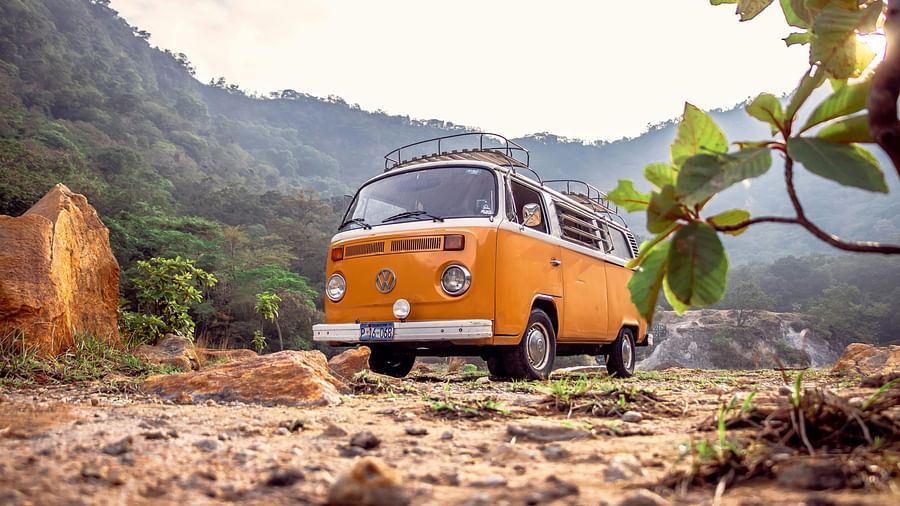 A vintage yellow and white Volkswagen bus parked on a dirt road with mountains in the background. - Bangalore to Goa on road