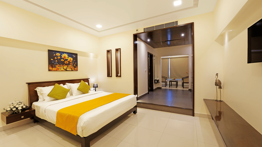 A Premium Room at Clover - A Rivido Hotel, featuring a neatly-made bed, a floral painting above the headboard, a decorative bird showpiece, and a large open doorway.