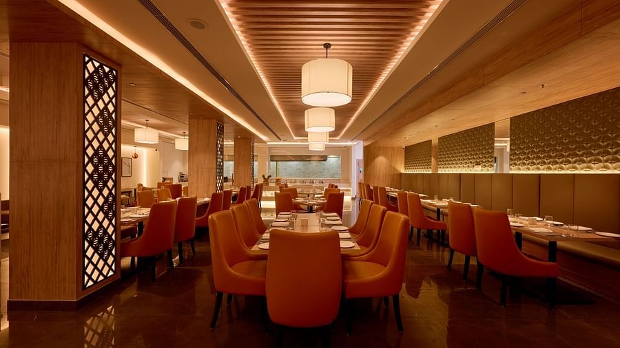 An image of our restaurant with orange chairs placed around tables under chandeliers 