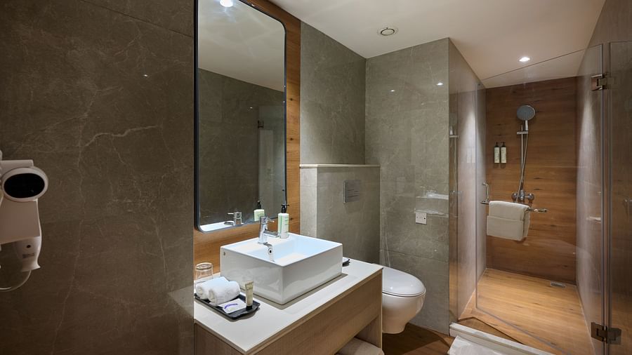 A hotel bathroom featuring a spacious sink, a wall-mounted mirror, and an enclosed shower cubicle