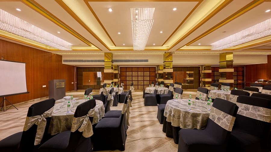 An image of a hall with blue chairs, round tables and a wall-mounted projector screen