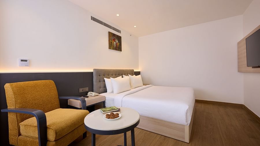 A hotel room captured from a side angle, featuring a bed, a chair, a coffee trading, and soft, ambient lighting