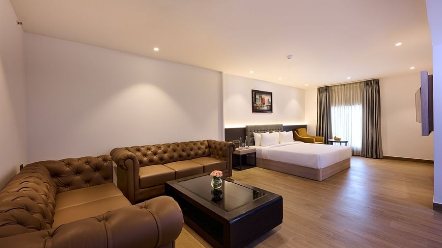 A hotel suite featuring a bed adjacent to a sofa, with a window that bathes the room in natural light