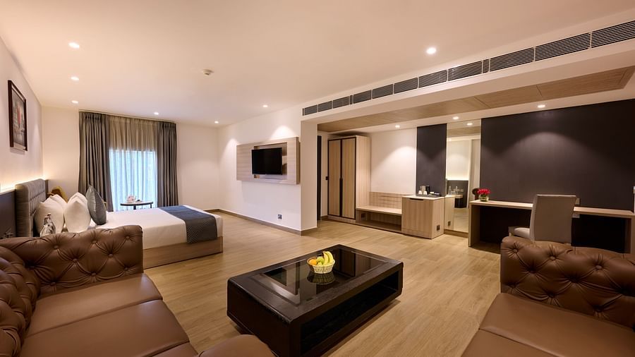 A hotel room equipped with a large bed, cosy sofas, and a television