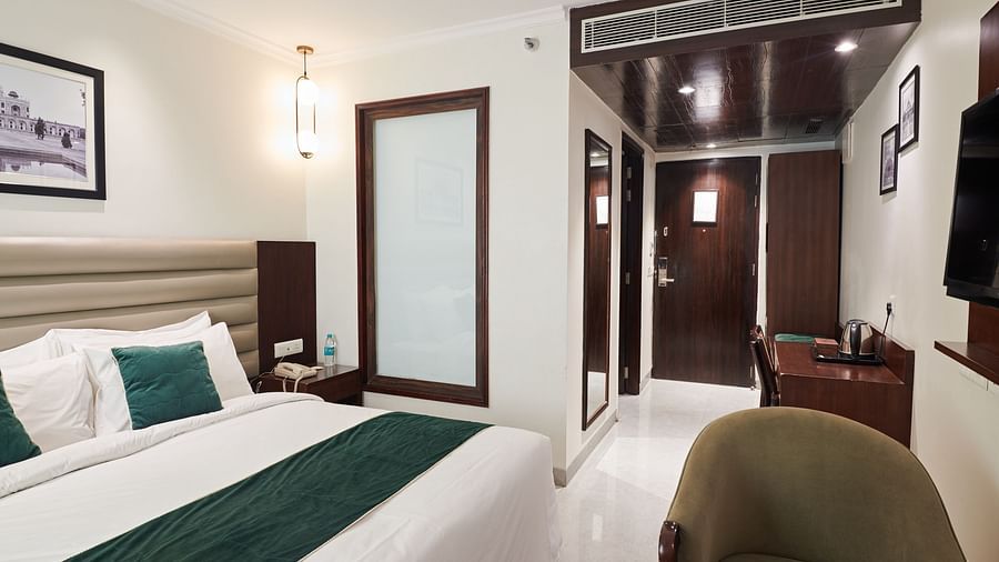An image of a hotel room with a large bed, a green chair and a wall-mounted television - Deventure Sarovar Portico, Patel Nagar
