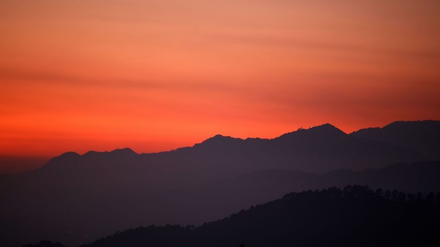  Soft pastel hues of sunset paint the sky, casting a gentle glow over the silhouetted mountain ranges, creating a serene and tranquil landscape, possibly a view from the resort