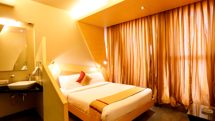 Cosy attic-style bedroom at Dragonfly Hotels with a sloped ceiling, double bed, warm lighting, and large curtained windows.