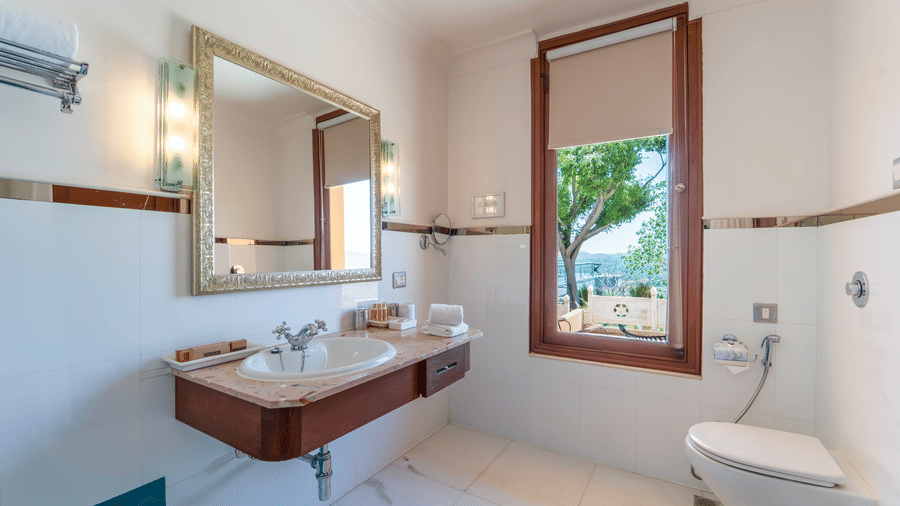 A clean white marble bathroom featuring a wall-mounted vanity and a window looking out toward trees - Fateh Garh, Udaipur